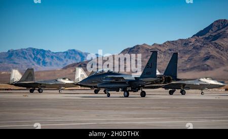 Un avion de chasse F-15E Strike Eagle affecté au 336e Escadron de chasse à la base aérienne de Seymour Johnson, en Caroline du Nord, des taxis devant des avions de chasse F-22 Raptor, affecté au 525e Escadron de chasse, base interarmées Elmendorf-Richardson, en Alaska, pendant le Red Flag 21-1 à Nellis AFB, Nevada, le 4 février 2021.Le drapeau rouge se concentre sur l'élaboration de l'état d'esprit des chasseurs de guerre, qui est l'idée que l'entraînement ensemble construit une force conjointe et de coalition létale, résiliente et rapidement adaptable. Banque D'Images