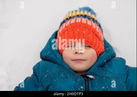 Petit garçon en bonnet tricoté faisant des anges de neige Banque D'Images