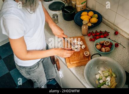 Une femme coupe des champignons sur une planche à découper dans la cuisine de la maison Banque D'Images