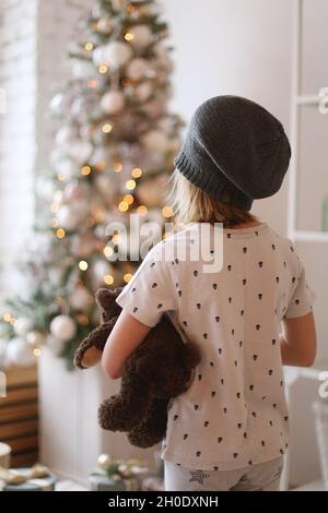un enfant dans un chapeau se tient devant un arbre de noël Banque D'Images