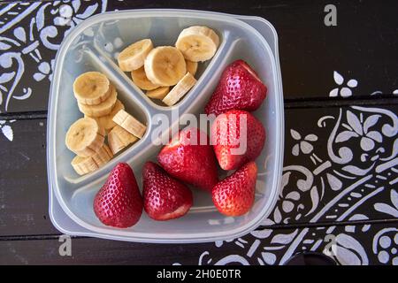 en-cas de fruits sains pour les enfants à emporter à l'école.Banane et fraise dans un bol sur une table en bois peinte en noir.Horizontale Banque D'Images