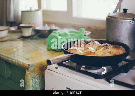 Une poêle à frire avec des tourtes rudes cuites sur la cuisinière à gaz et une vieille table avec des plats Banque D'Images