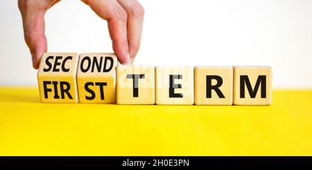 Symbole du premier ou du deuxième terme.L'homme d'affaires tourne des cubes en bois, change les mots du premier terme au deuxième terme.Belle table jaune, fond blanc.Buline Banque D'Images