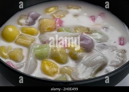 Vue rapprochée de délicieux desserts thaïlandais faits maison boules de riz collantes avec du ginkgo et de la viande de noix de coco dans le lait de coco dans un bol noir. Banque D'Images