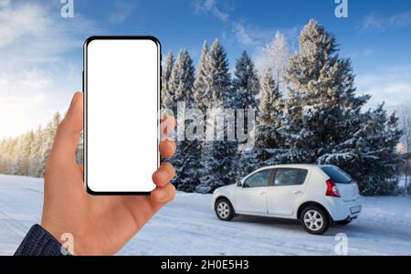 Main avec un téléphone sur l'arrière-plan d'une voiture derrière une route d'hiver.Écran vide, vous pouvez ajouter votre contenu Banque D'Images