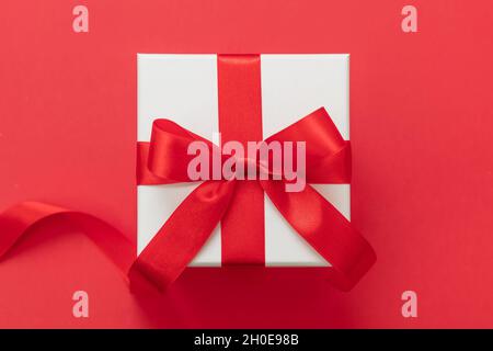 Boîte cadeau de Noël couleur blanche, noeud avec ruban rouge sur fond rouge, surprise de la Saint-Valentin, cadeau de Noël, décoration en satin Banque D'Images