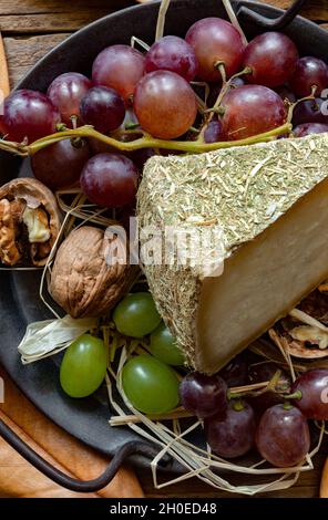 tranche de fromage pecorino avec du foin de montagne, sur fond automnal avec des raisins noirs Banque D'Images