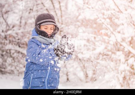 L'enfant joue des boules de neige sur le fond d'une forêt de neige. Banque D'Images