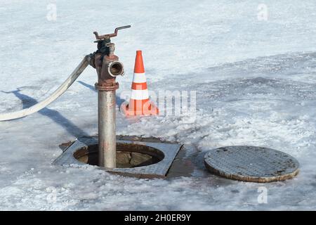 Un trou d'homme ouvert, une pompe et un cône de circulation en hiver. Banque D'Images