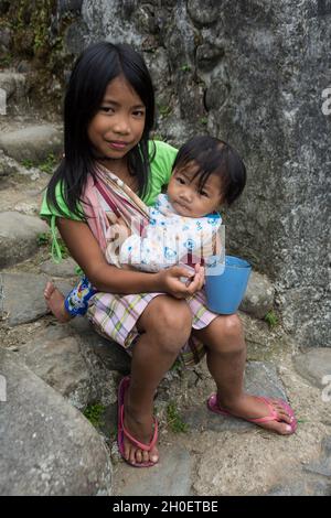 Jeune fille philippine tenant sa petite sœur sur ses genoux tout en la nourrissant.Village de Batad, province d'Ifugao, Philippines Banque D'Images