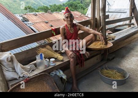 Ancien Ifugao en costume traditionnel assis sur un banc en bois sur la véranda de sa maison dans le village de Batad, province d'Ifugao, Philippines Banque D'Images