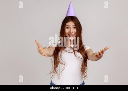 Femme avec nimbus gardant les mains ouvertes pour embrasser, donnant un accueil chaleureux, salutation et partage de l'amour, en portant blanc style décontracté T-shirt.Prise de vue en studio isolée sur fond gris. Banque D'Images