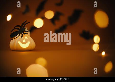 Arrière-plan de Halloween.Citrouille en forme de citrouille lumineuse avec décorations en forme d'araignée sur fond orange foncé avec lumières magiques et chauves-souris noires volantes.Happ Banque D'Images