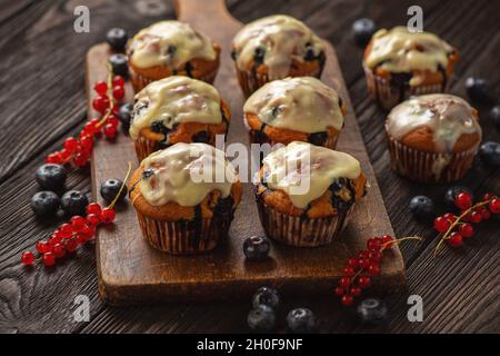 Muffins faits maison aux raisins de Corinthe rouges et aux bleuets, recouverts de garniture au chocolat blanc. Banque D'Images
