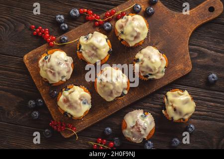 Muffins faits maison aux raisins de Corinthe rouges et aux bleuets, recouverts de garniture au chocolat blanc. Banque D'Images