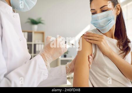 Infirmière en gants et masque facial donnant un vaccin contre la grippe ou Covid 19 à un jeune patient Banque D'Images