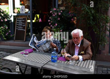 Une dame lit un journal tandis que l'homme regarde son smartphone à côté d'un café restaurant en France Banque D'Images