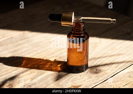 Flacon en verre ambré foncé avec compte-gouttes pour l'huile, la lotion ou le sérum sur un fond en bois vieilli avec une ombre dure de feuilles de palmier tropicales.Présentation d'un produit cosmétique.Aménagement du salon de beauté . Banque D'Images