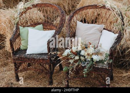 Deux chaises en osier avec coussins et bouquet de fleurs. Chaises en rotin avec des balles de paille en arrière-plan. Style boho Banque D'Images