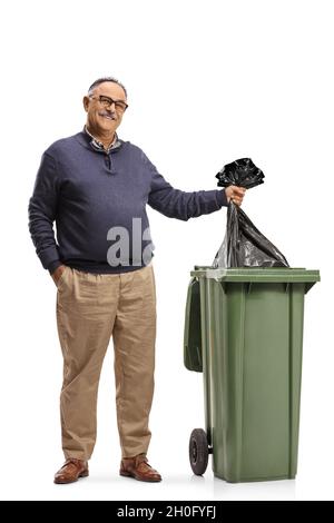 Homme mûr debout à côté d'une poubelle et jetant un sac en plastique à l'intérieur isolé sur fond blanc Banque D'Images