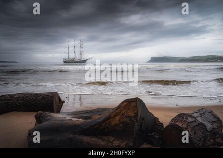 Ciel de tempête spectaculaire sur un grand navire ancré près de la côte d'Irlande du Nord, Fair Head à distance, vu de l'arrière du bois de dérive sur une plage Banque D'Images