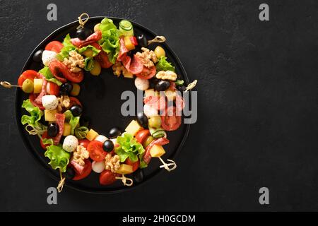 La nourriture de Noël est une couronne d'en-cas, de canapés, de tomates, d'olives, de légumes, de mozzarella pour les fêtes de Noël sur fond noir. Vue de Banque D'Images