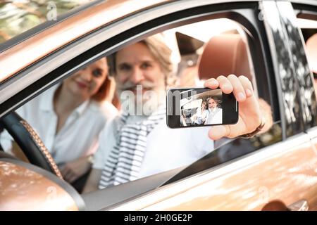 Heureux couple d'âge mûr en voiture sur écran de téléphone mobile Banque D'Images