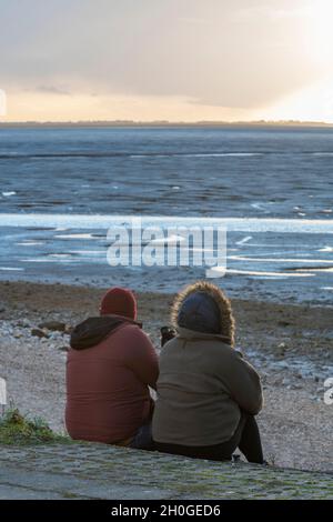 couple assis sur la plage de snettisham dans le nord de norfolk à marée basse lors d'une soirée d'automne fraîche qui donne sur la mer en profondeur en pensant à l'ambiance de coucher de soleil Banque D'Images