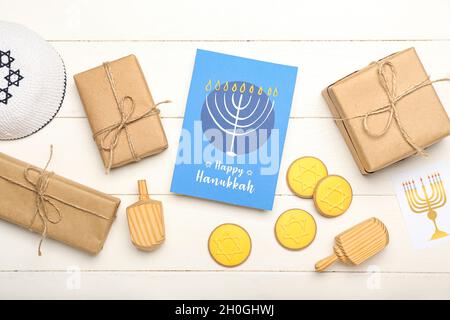 Différents symboles de Hanukkah, cadeaux et carte de vœux sur fond blanc en bois Banque D'Images