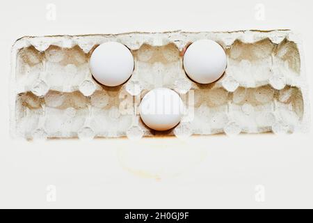 Trois œufs blancs dans un plateau en carton sur fond blanc Banque D'Images