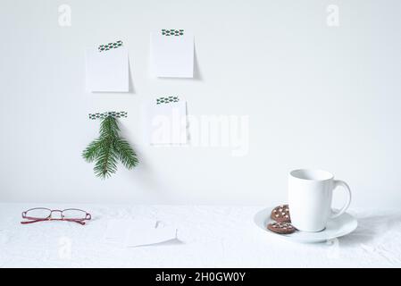 Petit déjeuner de fête encore vivant.tasse de café avec biscuits, verres sur le bureau.branche de sapin, blocs-notes vides maquette accrochée sur le mur blanc.décor de Noël.W Banque D'Images