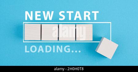 Mots nouveau départ avec une barre de chargement, la main met le dernier cube en bois sur le fond bleu Banque D'Images