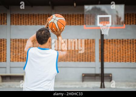 vue arrière d'un joueur de basket-ball tenant le ballon tout en sautant le tir dans le panier Banque D'Images