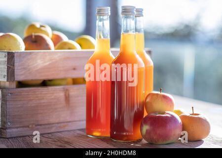 Jus de pomme naturellement nuageux, fait maison dans une bouteille de jus avec des pommes dans une caisse de pomme avec lumière d'automne Banque D'Images