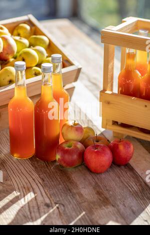 Jus de pomme naturellement nuageux, fait maison dans une bouteille de jus avec des pommes dans une caisse de pomme avec lumière d'automne Banque D'Images