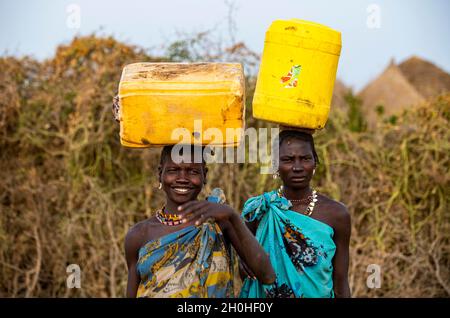 Femmes traditionnelles habillées transportant des conteneurs d'eau, tribu Jiye, État d'Equatoria orientale, Soudan du Sud Banque D'Images