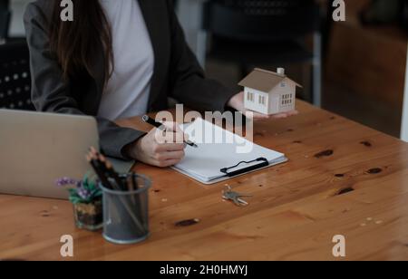 Gros plan maison modèle miniature sur la table de realtor, femme d'affaires agent immobilier courtier écrire avec des documents, prendre des notes, préparer le contrat pour Banque D'Images