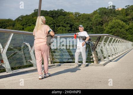 Homme senior souriant avec tapis accueille une femme marchant sur la passerelle Banque D'Images