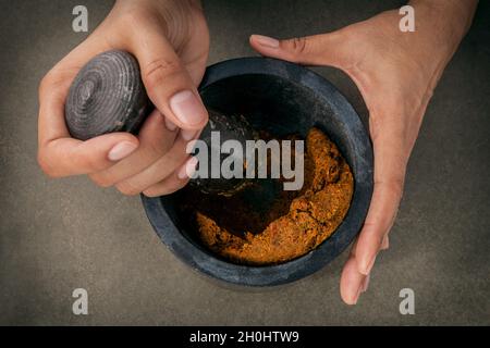 Les femmes occupent moins de mortier et d'épices et de pâte de curry rouge thaï de l'ingrédient alimentaire populaire sur fond de béton foncé. Banque D'Images