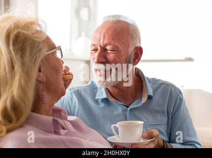 Couple senior assis sur un canapé parlant et buvant du café.Ambiance affectueuse à la maison Banque D'Images