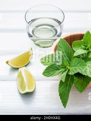 Ingrédients pour faire le mojito feuilles de menthe poivrée, lime slices et vodka sur table en bois blanc, arrière-plan. Selective focus profondeur de champ . Banque D'Images