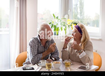 Couple de personnes âgées assis à la table à manger, boire du café et manger des biscuits Banque D'Images
