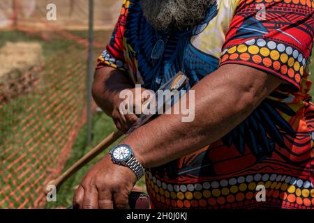 Eungella, Queensland, Australie - octobre 2021 : un aborigène barbu portant une montre et une chemise colorée brandissant une hache à une reconstitution de pays Banque D'Images