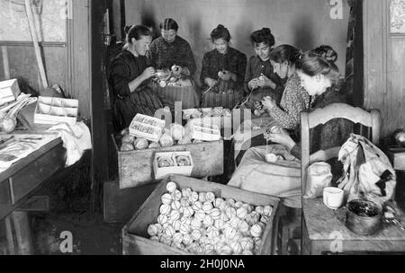 Les travailleurs à la maison couvrent les boules d'arbre de Noël avec du fil d'or et des fils de verre filé.(photographie non datée) [traduction automatique] Banque D'Images