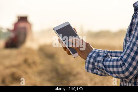 Gros plan des mains du fermier tenant la tablette devant la moissonneuse-batteuse dans le champ de soja Banque D'Images