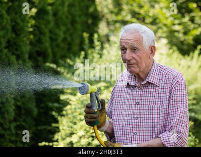 Homme expérimenté arrosoir des plantes dans le jardin avec pistolet à main sur le tuyau.Prendre soin de l'arrière-cour Banque D'Images