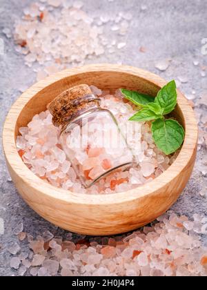 Libre de sel rose de l'Himalaya en bouteille et bol en bois avec feuilles de menthe poivrée sur fond de pierre. Sel de l'himalaya utilisé pour la cuisson et à bat Banque D'Images