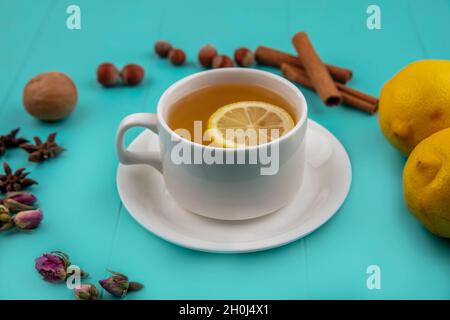 vue latérale d'une tasse de thé avec une tranche de citron et de cannelle avec des noix de noyer citrons et des fleurs sur fond bleu Banque D'Images