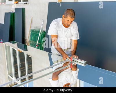 Un homme coupant verre de miroir avec coupe-verre à utiliser dans la production locale de meubles Banque D'Images