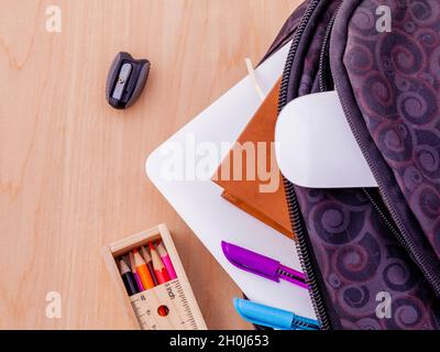 Sac à dos avec des fournitures scolaires coffre,livre,souris,fixes,stylo, règle et crayon de couleur sur la table en bois . Banque D'Images